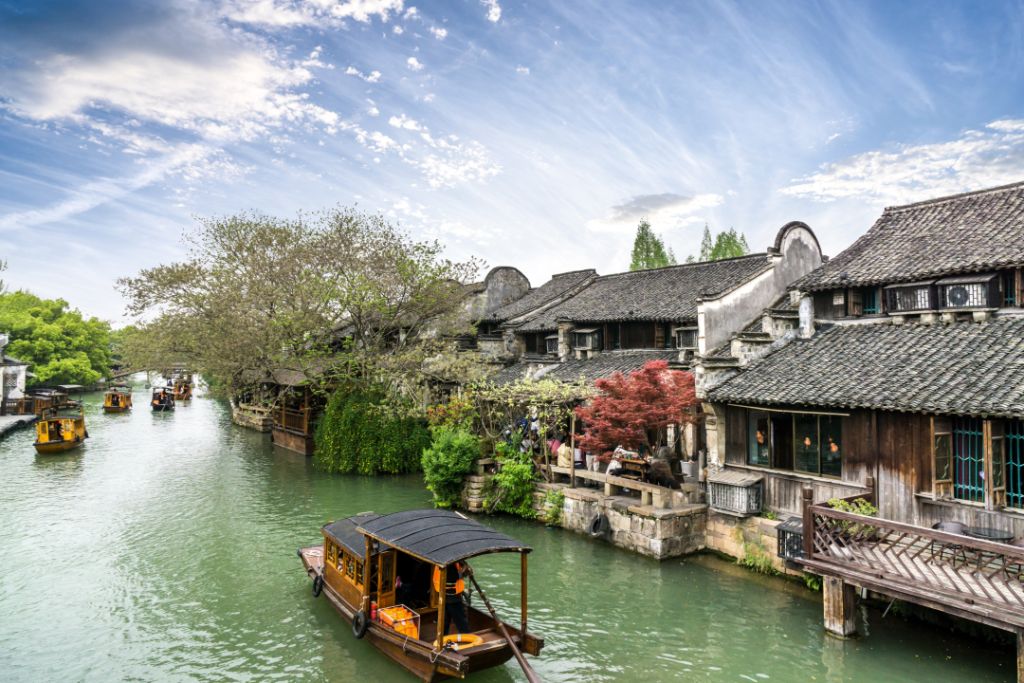 Image shows a scene in China of traditional houses by a water course and a boat.