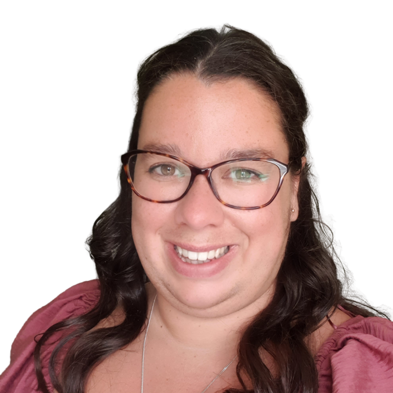 Woman with long, wavy dark hair and glasses, smiling at the camera. She is wearing a pink top and a necklace, and the background is plain white.